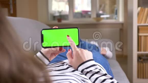 特写后景拍摄的女性网络在手机与绿色屏幕保持它水平躺在沙发上视频的预览图