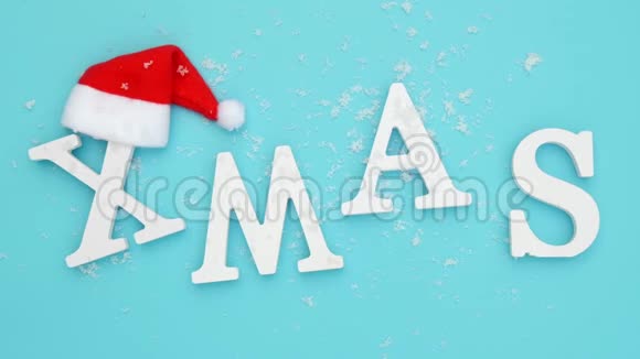 圣诞节从卷白色字母红色圣诞老人帽子和降雪蓝色背景概念圣诞快乐顶级视频的预览图