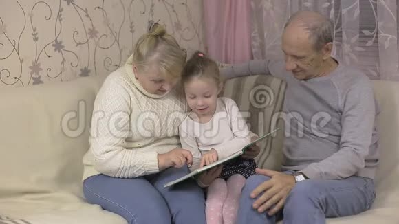 小女孩去看望祖父母和他们一起坐在沙发上看书视频的预览图