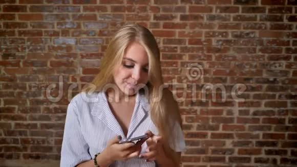 年轻的白种人金发美女使用智能手机显示智能手机屏幕蓝色屏幕肖像砖墙视频的预览图