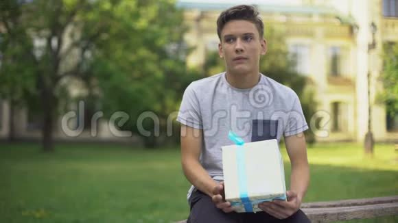 紧张的少年坐在长凳上拿着礼品盒等着女朋友视频的预览图