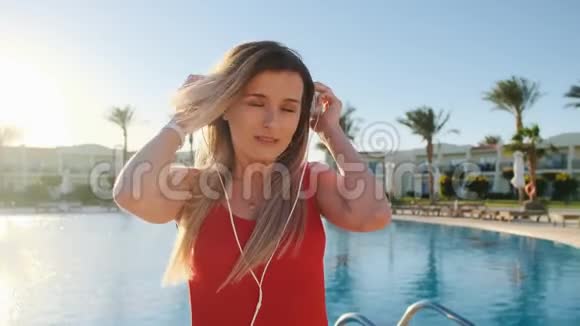 穿着红色泳衣和耳机在智能手机上跳舞和听音乐的漂亮女孩的肖像视频的预览图