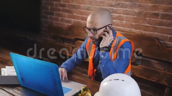 stroyploshadka的建筑师在笔记本电脑后面工作带着技术文档在电话里交谈视频的预览图