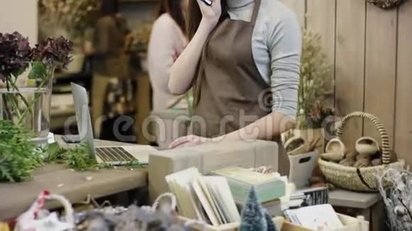 年轻的女人在花店工作通过电话交谈在她的笔记本电脑上打字相机从底部进入视频的预览图