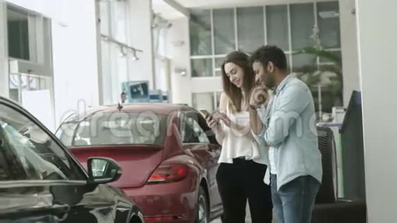 帅哥和美女在汽车陈列室使用智能手机视频的预览图