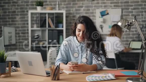 使用智能手机触摸屏幕的快乐女孩在办公桌前工作视频的预览图