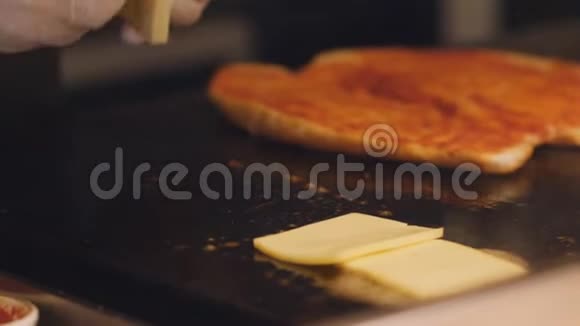 厨师把奶酪片分解在一个热金属盘子里在厨房准备三明治吃早餐视频的预览图