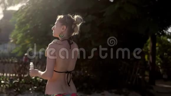 女人的身体油穿比基尼的年轻女人给她的身体涂上奶油绿树树背景视频的预览图