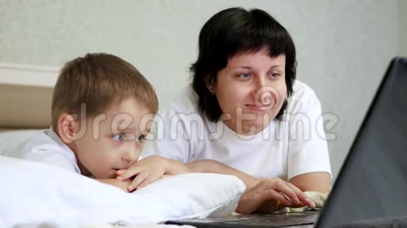幸福家庭妈妈和孩子躺在床上高兴地看着笔记本电脑屏幕一边互相交谈视频的预览图