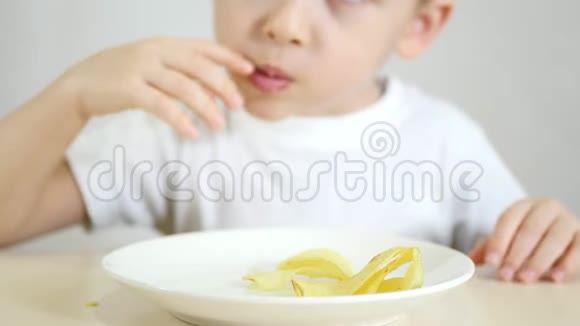 一个孩子正吃着白色盘子里的薯片坐在桌子旁特写聚焦相机瞄准一个装有视频的预览图