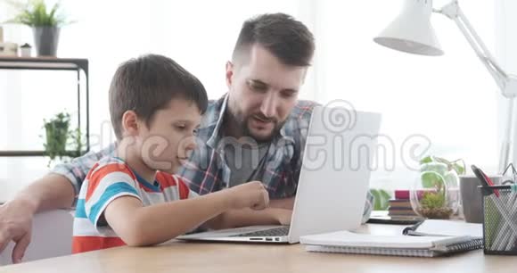 父亲和儿子在家里用笔记本电脑视频的预览图