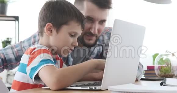 父亲和儿子在家里用笔记本电脑视频的预览图