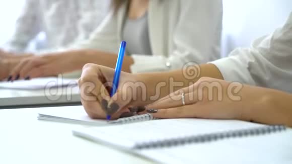 在教室里用钢笔在笔记本上书写年轻男女学生的手视频的预览图
