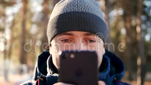 一个穿着温暖衣服的男人在寒冷的季节用智能手机看着手机屏幕特写镜头视频的预览图