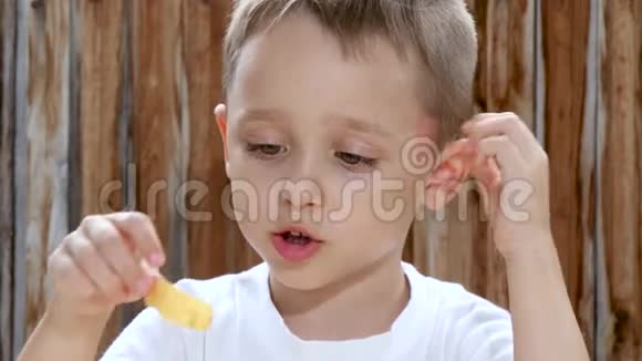 一个孩子在木墙的背景下坐在一张桌子旁一边高兴地吃薯片视频的预览图