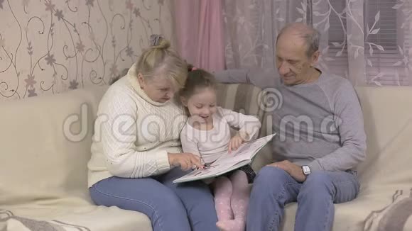 小女孩去看望祖父母和他们一起坐在沙发上看书视频的预览图
