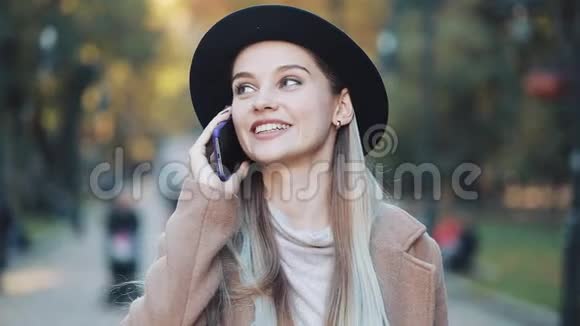 一位年轻的美女在秋天的公园里在一片黄叶的背景下一边用手机视频的预览图