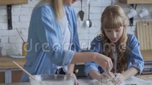 妈妈和女儿正在厨房里做面团女人把手上的面团放在木桌上家庭食品概念视频的预览图