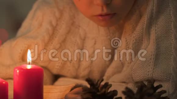 女孩看着松果蜡烛燃烧在附近圣诞工艺品特写视频的预览图