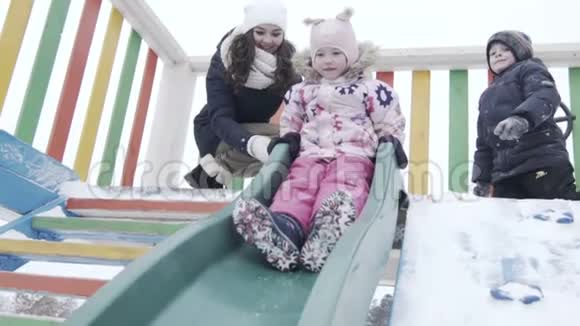 滑动冬季公园孩子们滑梯女孩在冬天的公园里滑下来视频的预览图