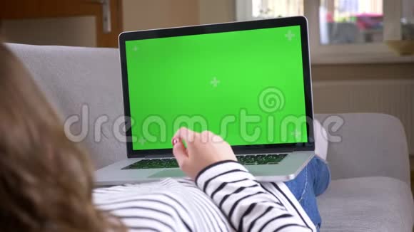笔记本电脑上女性观看广告的特写后景拍摄沙发上有绿色的彩色屏幕视频的预览图