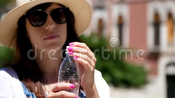 意大利威尼斯2018年7月7日一位戴着太阳眼镜和帽子的年轻女子从瓶子里喝着清澈干净的高山水视频的预览图