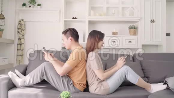 亚洲夫妇使用智能手机检查社交媒体在家里的客厅甜蜜的夫妇享受爱情的时刻视频的预览图