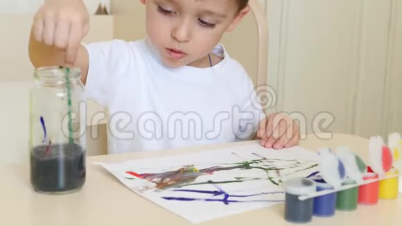 孩子在桌旁的一张白纸上画了一幅画那个男孩把刷子浸入水中视频的预览图