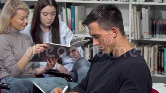 英俊的男学生微笑着对着相机一边在图书馆做作业视频的预览图