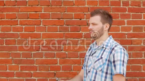 时尚时尚的男人留着胡子在砖墙上抽着一根带子复制空间慢节奏外面视频的预览图