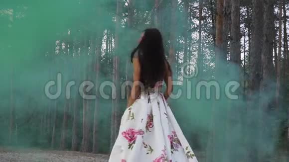 穿着一件衣服的可爱女孩在森林的背景下走在彩色烟雾中视频的预览图