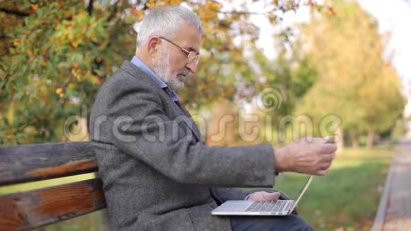 高级商人在外面用笔记本电脑穿灰色夹克的老人在公园里用笔记本电脑视频的预览图