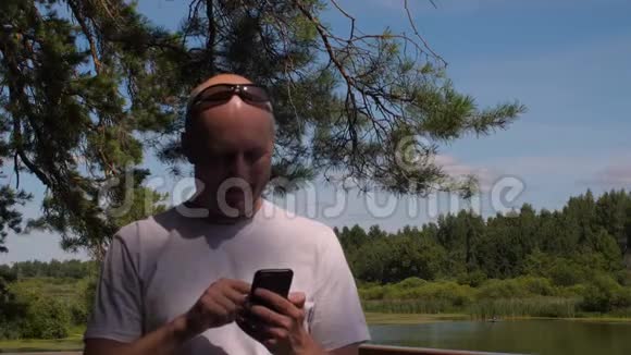 帅哥在树和池塘的景观上打手机视频的预览图