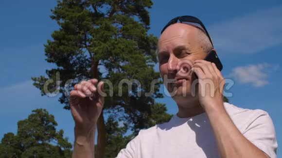 戴眼镜的秃头男子在夏季公园背景下通过手机通话视频的预览图