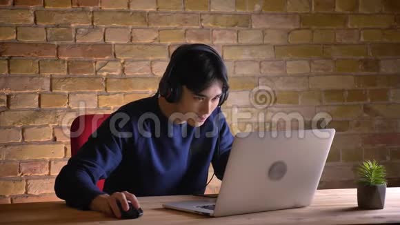 年轻的韩国商人戴着耳机在笔记本电脑上浏览的特写肖像因为这件事而兴奋起来视频的预览图