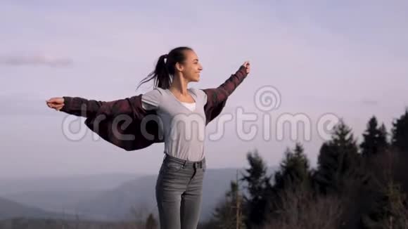 年轻的女徒步旅行者站在山岭边缘站在夕阳的背景下视频的预览图