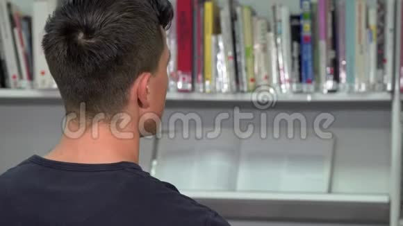 一名男子在图书馆书架上看书的后景镜头视频的预览图