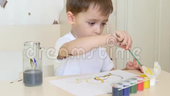 一个孩子坐在桌子旁的一张白纸上用油漆画画这个男孩用刷子和水粉视频的预览图
