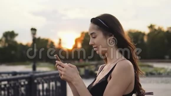 美丽的女孩模特在手机特写日落时看信息可爱地微笑视频的预览图