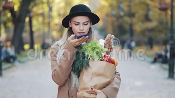 年轻漂亮的女人穿着时髦的外套走在街上拿着一包产品和她说话视频的预览图