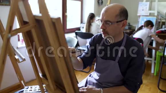 成年男性眼镜画家用画笔和油画画一幅画艺术观念富有创造力的快乐画家视频的预览图