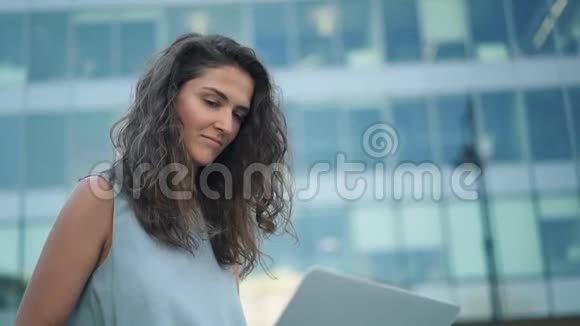 穿着蓝色裙子的漂亮年轻女人用她的电脑在市中心视频的预览图