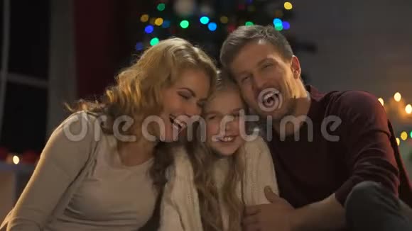 年轻的家庭拥抱欢笑看着镜头圣诞灯光闪闪发光视频的预览图