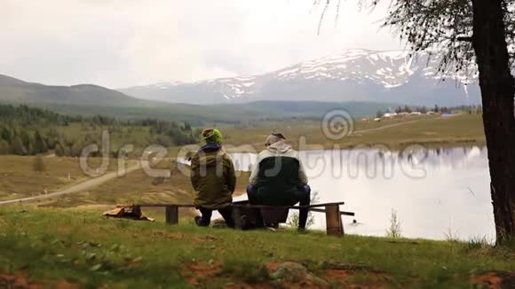 两个成年人的后景坐在长凳上花时间环顾山湖美景视频的预览图