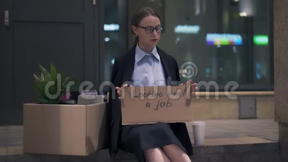 坐在街上找工作标志的坐着硬纸板的女人心烦意乱视频的预览图