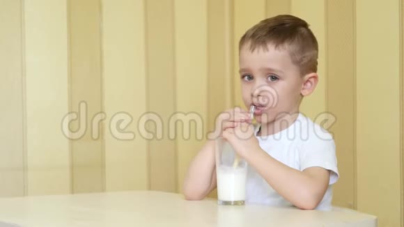 这个孩子高兴地喝着杯子里的牛奶通过一根稻草坐在桌子上伸出大拇指视频的预览图