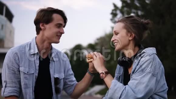 年轻人一起咬一个大汉堡分享食物傍晚公园里的黄昏情侣约会花时间视频的预览图