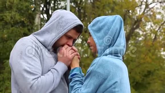 在外面寒冷天气里穿运动服的年轻夫妇男人用呼吸温暖女孩双手视频的预览图