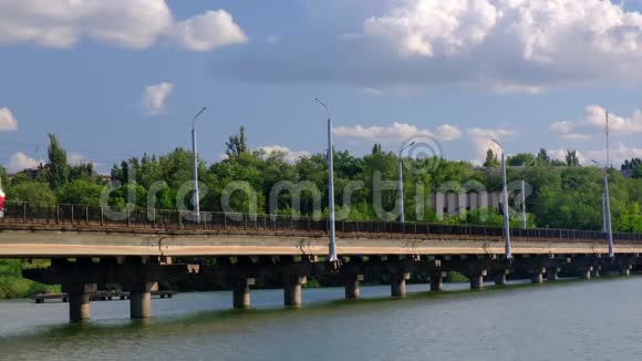 有轨电车在一个以绿树为背景的城市里沿着河上的桥行驶视频的预览图