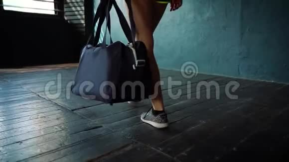 慢速运动适合年轻女性的腿带着袋子进入健身房并准备训练视频的预览图
